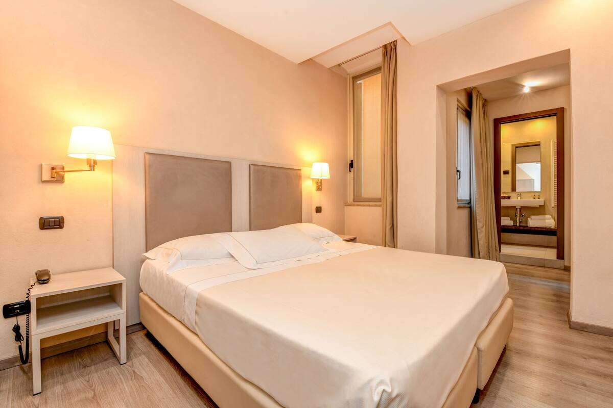 A hotel room with a large bed, bedside lamps, a nightstand, and a mirror.