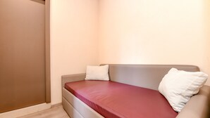 A small, single-bed room with a brown door, a red mattress, and two pillows. - Hotel Tripoli (Desenzano del Garda)