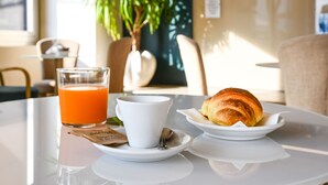 A breakfast setting with a glass of orange juice, a white cup, and a croissant on a white table. - Hotel Tripoli (Desenzano del Garda)