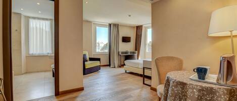 Habitación de hotel con piso de madera, una cama, un sofá, una mesa con lámpara y un televisor en la pared.