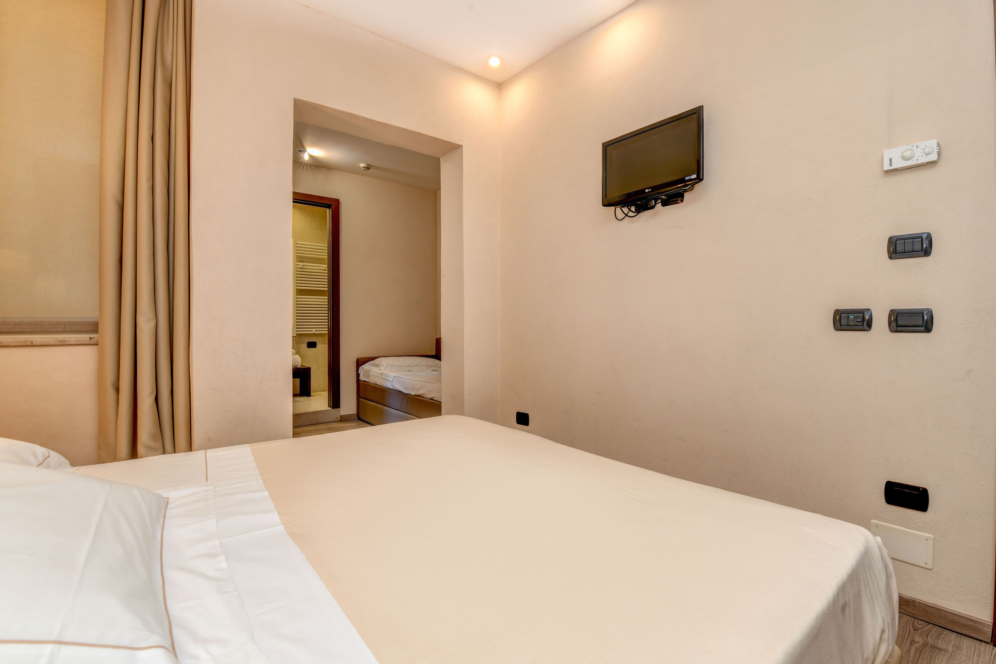Camera d'albergo con un letto grande, una televisione montata a parete e un bagno visibile attraverso una porta aperta.