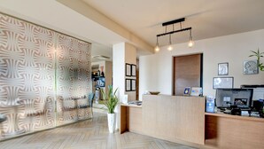 A modern reception area with a wooden reception desk, a patterned wall, and a potted plant. - Hotel Tripoli (Desenzano del Garda)