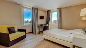 A hotel room with a bed, a sofa, a desk, and a TV. - Hotel Tripoli (Desenzano del Garda)
