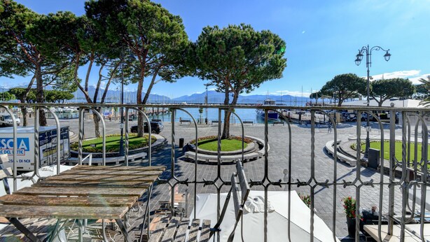 A waterfront promenade with a circular park, benches, and a metal railing. - Hotel Tripoli (Desenzano del Garda)