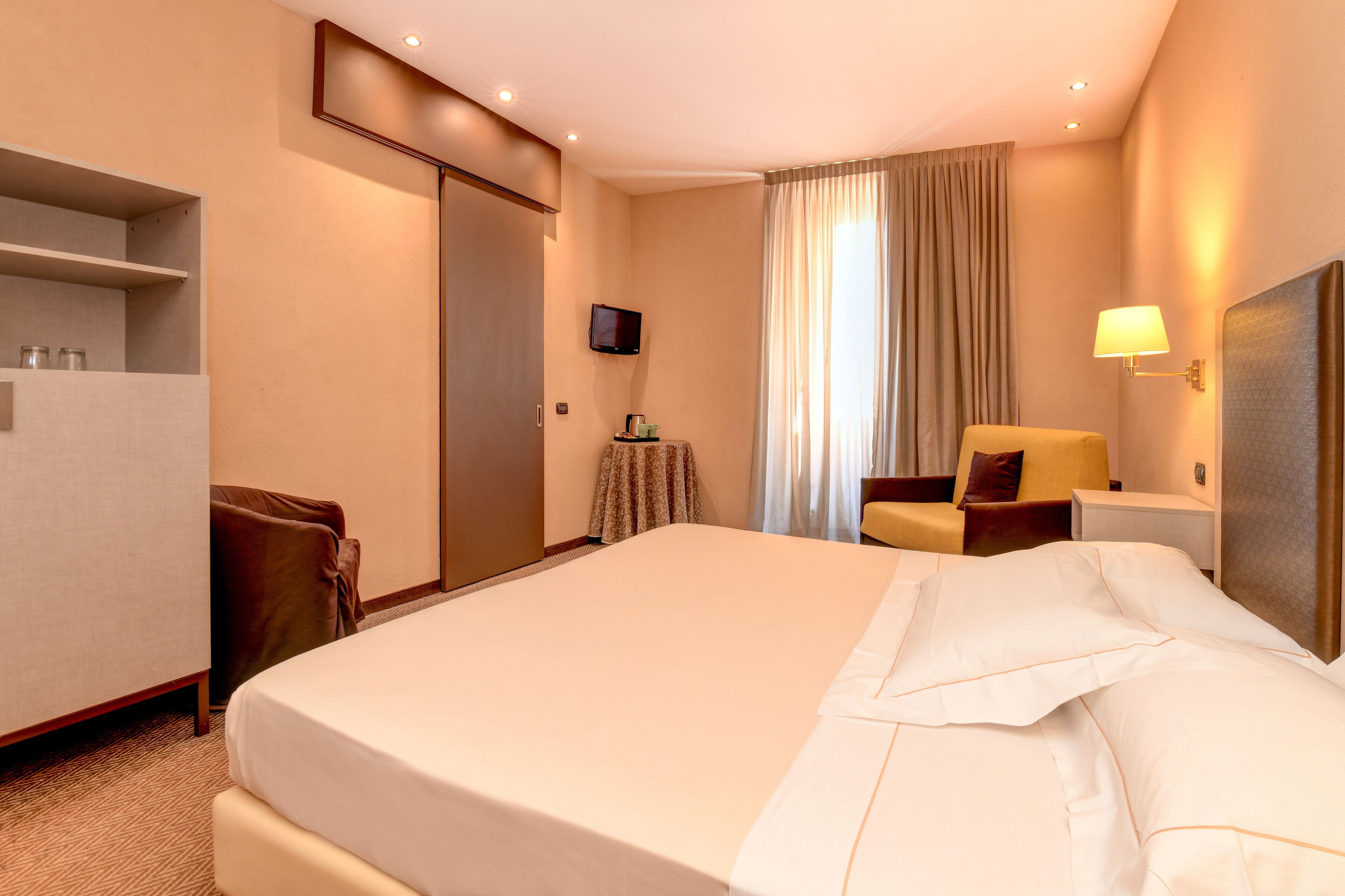 A hotel room with a large bed, a desk, a chair, a television, and a window with curtains.