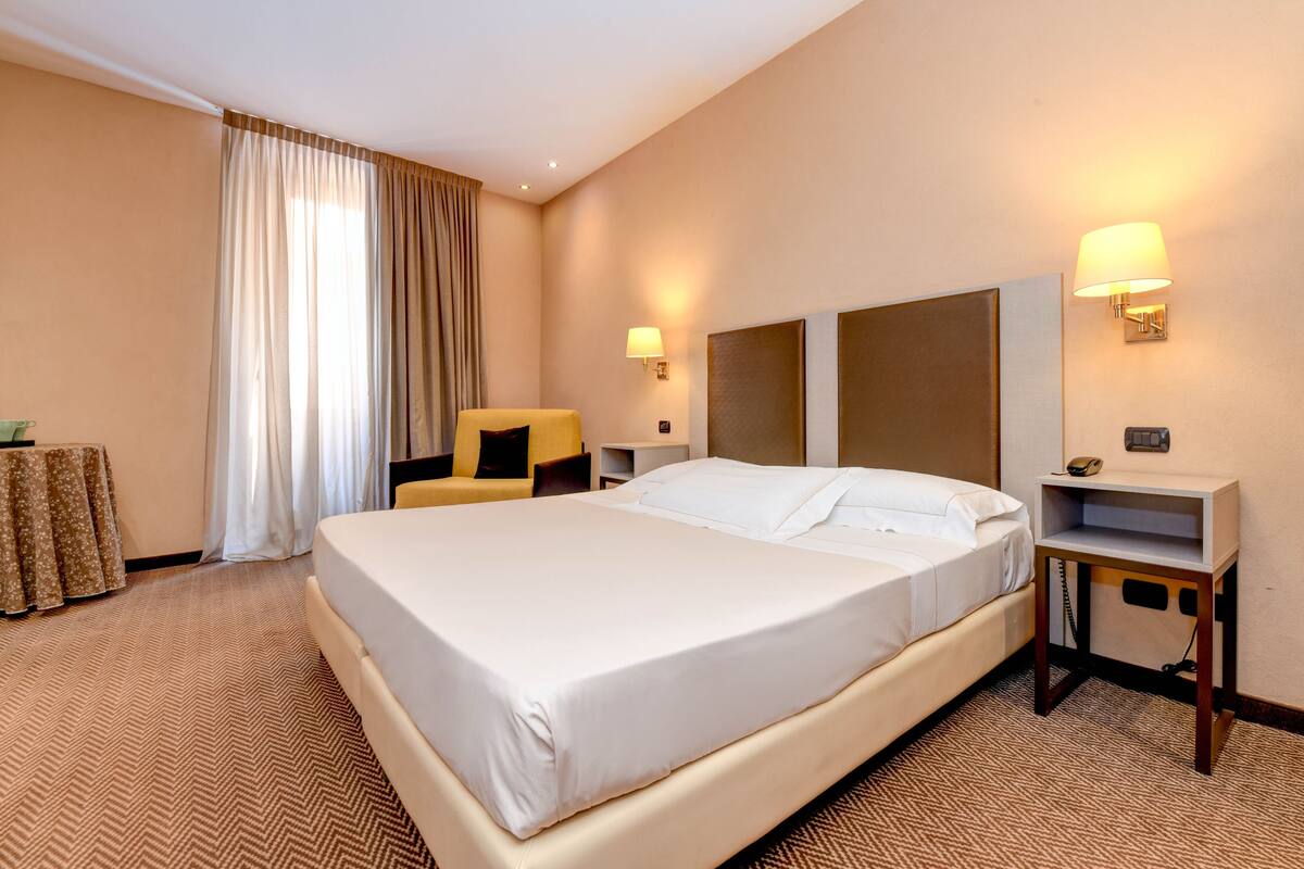 A hotel room with a large bed, a chair, a desk, and a lamp.