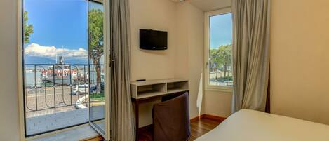 Une chambre d’hôtel dotée d’une grande fenêtre, d’un lit, d’un bureau avec une chaise et d’un téléviseur fixé au mur.