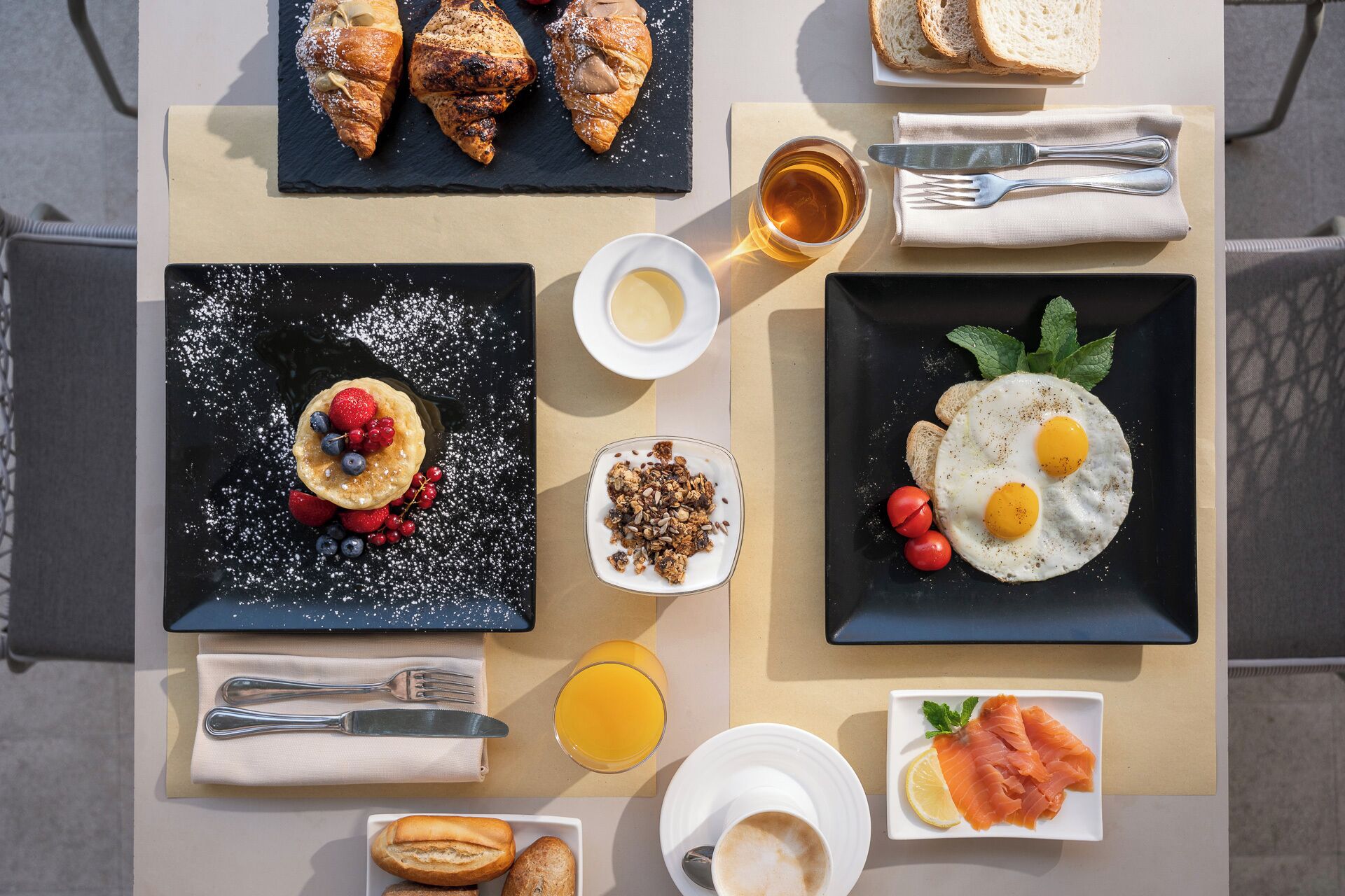 Un petit-déjeuner composé de croissants, d’œufs brouillés, de fruits rouges, de granola, de pain grillé, de saumon et de jus d’orange.