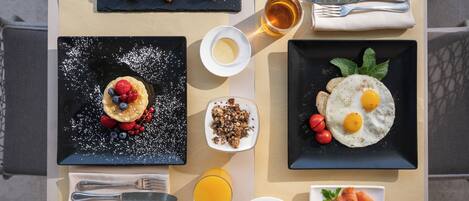 Un petit-déjeuner composé de croissants, d’œufs brouillés, de fruits rouges, de granola, de pain grillé, de saumon et de jus d’orange.
