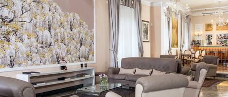 A spacious living room with a large floral mural, comfortable seating, a glass coffee table, and a bar area in the background.