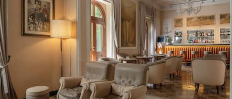 A luxurious hotel lobby with leather armchairs, a marble coffee table, a bar area with a wine selection, and classic decor.