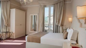 Habitación de hotel con una cama grande, una mesita de noche con lámpara, un armario y vistas al balcón exterior.