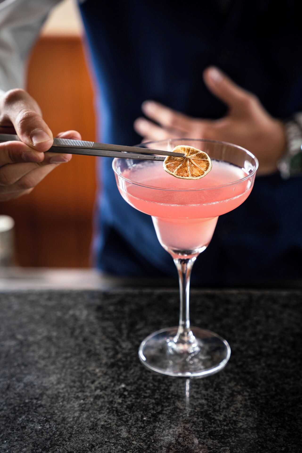 A cocktail in a martini glass with a dried orange slice garnish.
