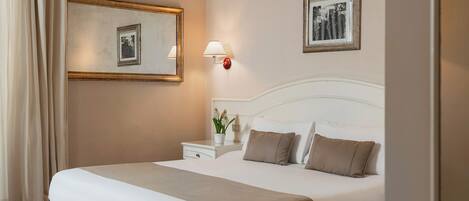 A hotel room with a large bed, a nightstand with a lamp, a mirror, and two framed pictures on the wall.