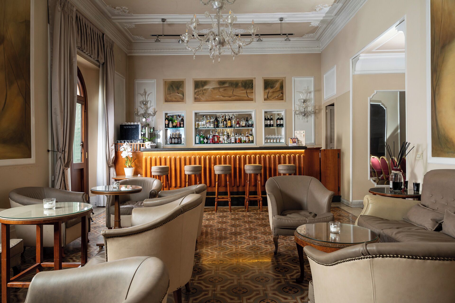 Zona de bar con barra, taburetes y una variedad de botellas. Varias áreas de estar con sillones de cuero y mesas.