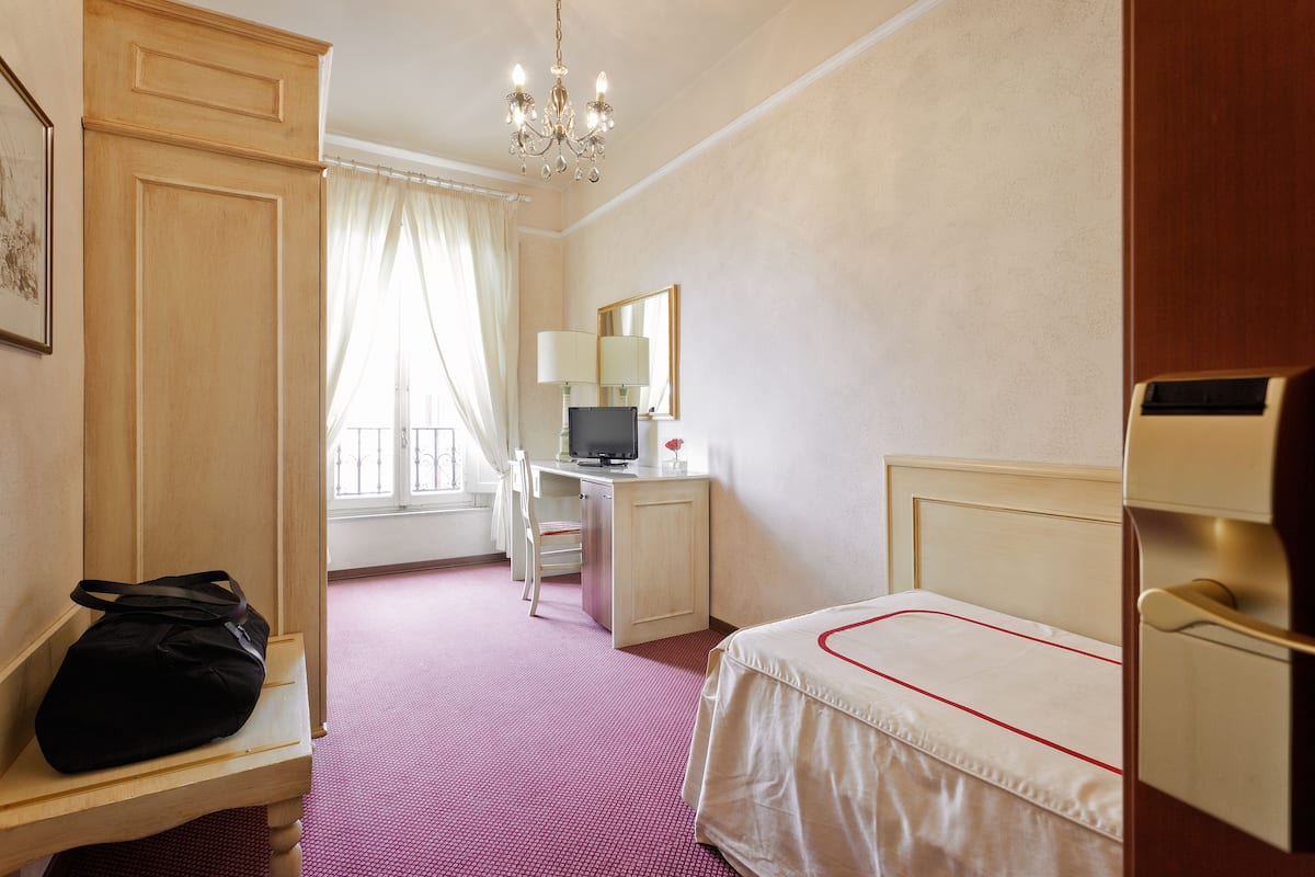 A hotel room with a bed, desk, chair, and a television.
