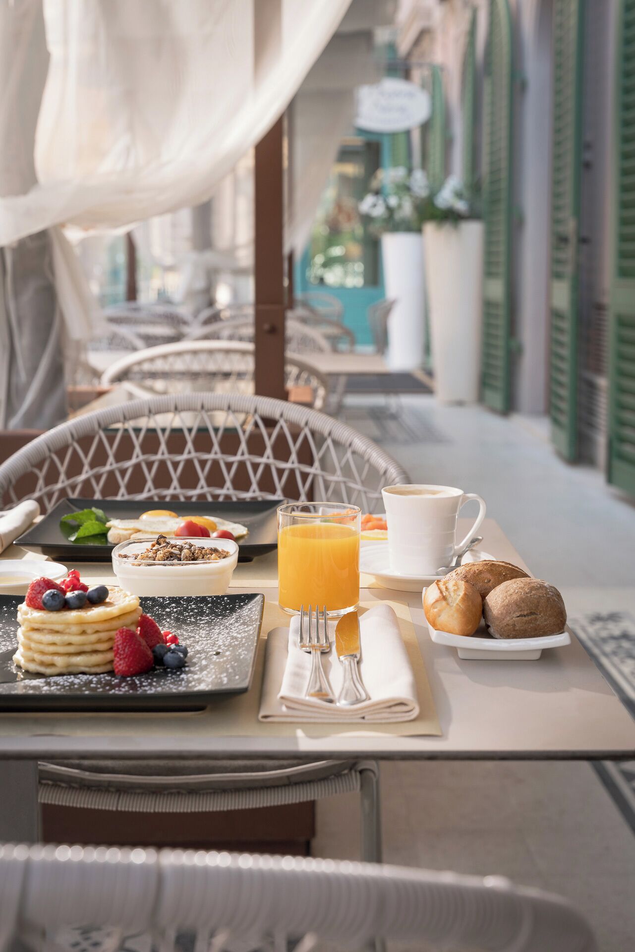 A breakfast table with pancakes, fruit, a glass of orange juice, a cup of coffee, and pastries.