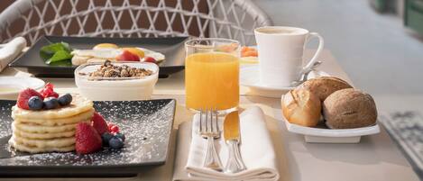 A breakfast table with pancakes, fruit, a glass of orange juice, a cup of coffee, and pastries.