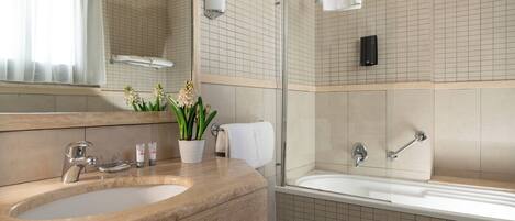 A bathroom with a sink, mirror, and bathtub. There are towels and a potted plant on the counter.