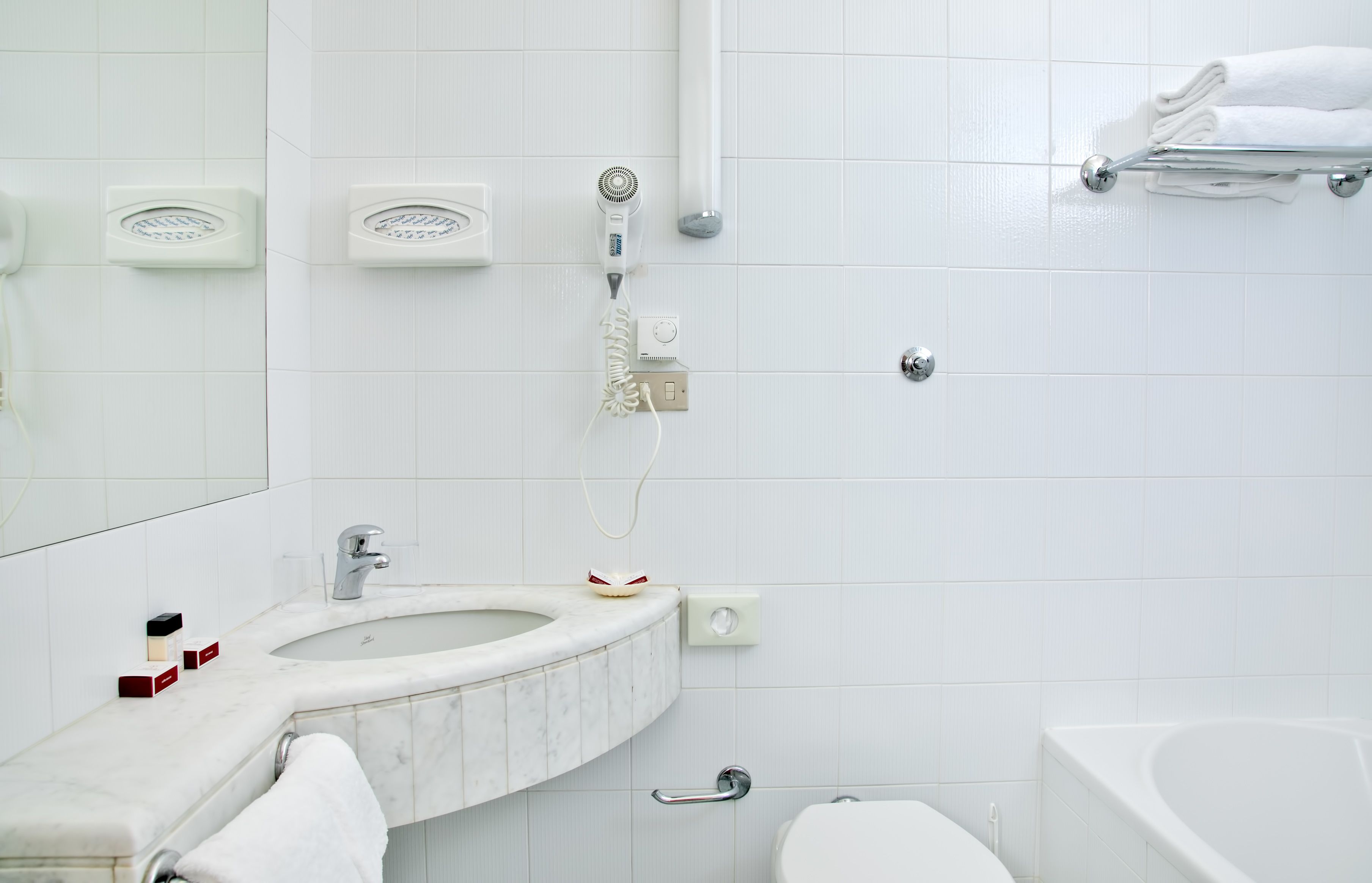 Un baño con lavamanos blanco, espejo y bañera. Hay dos toalleros, un cabezal de ducha de mano y un inodoro.