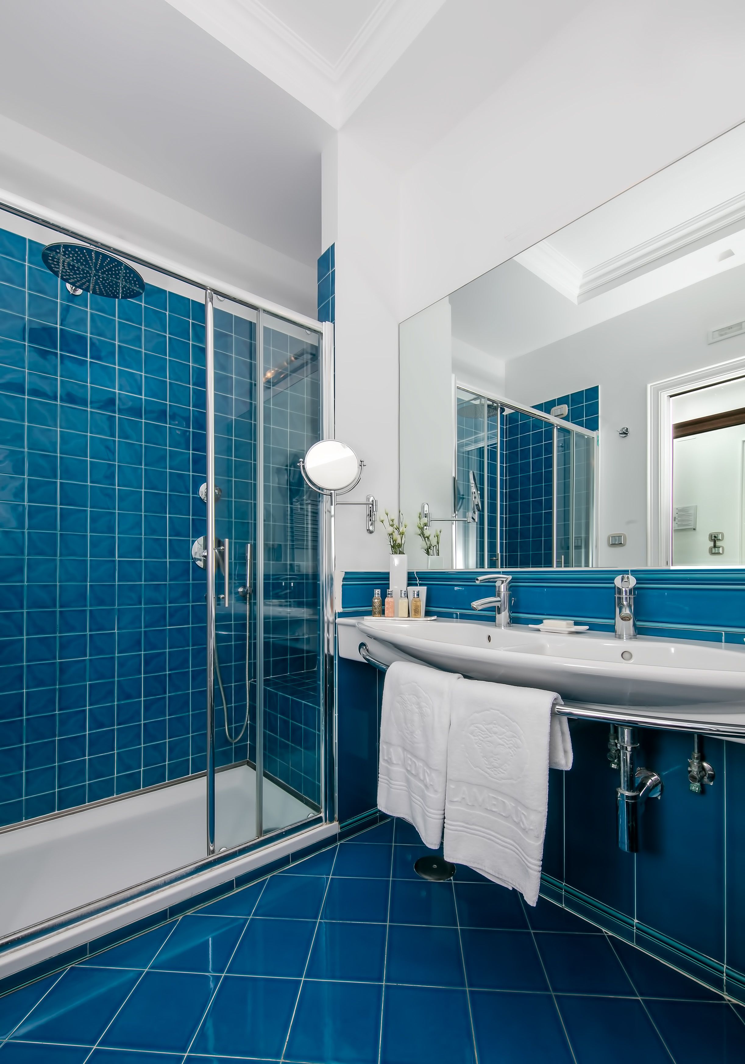 Une salle de bain avec une douche à parois de verre, un lavabo blanc avec un miroir et des murs recouverts de carreaux bleus.