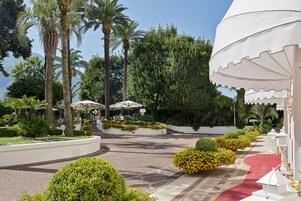 Un jardín ajardinado con palmeras, una alfombra roja y sombrillas blancas.
