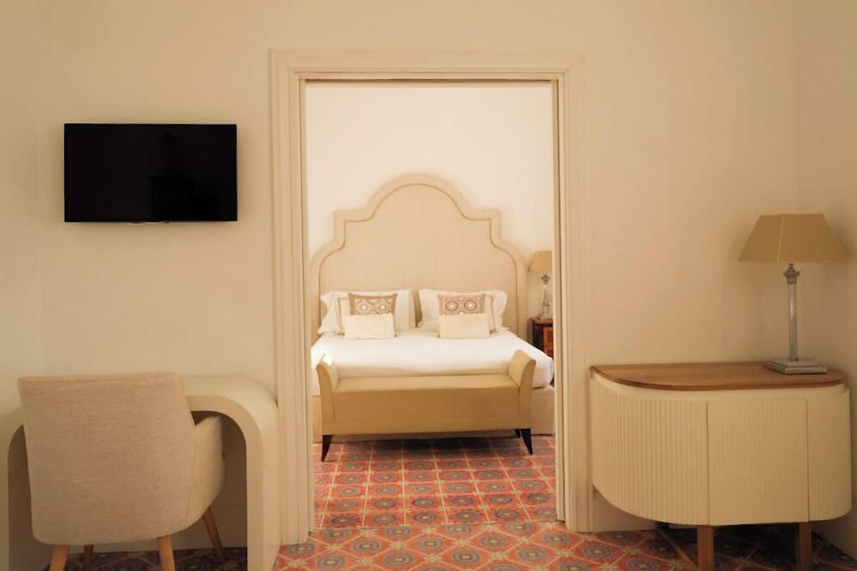 A hotel room with a bed, a TV, a desk, a chair, and a lamp.