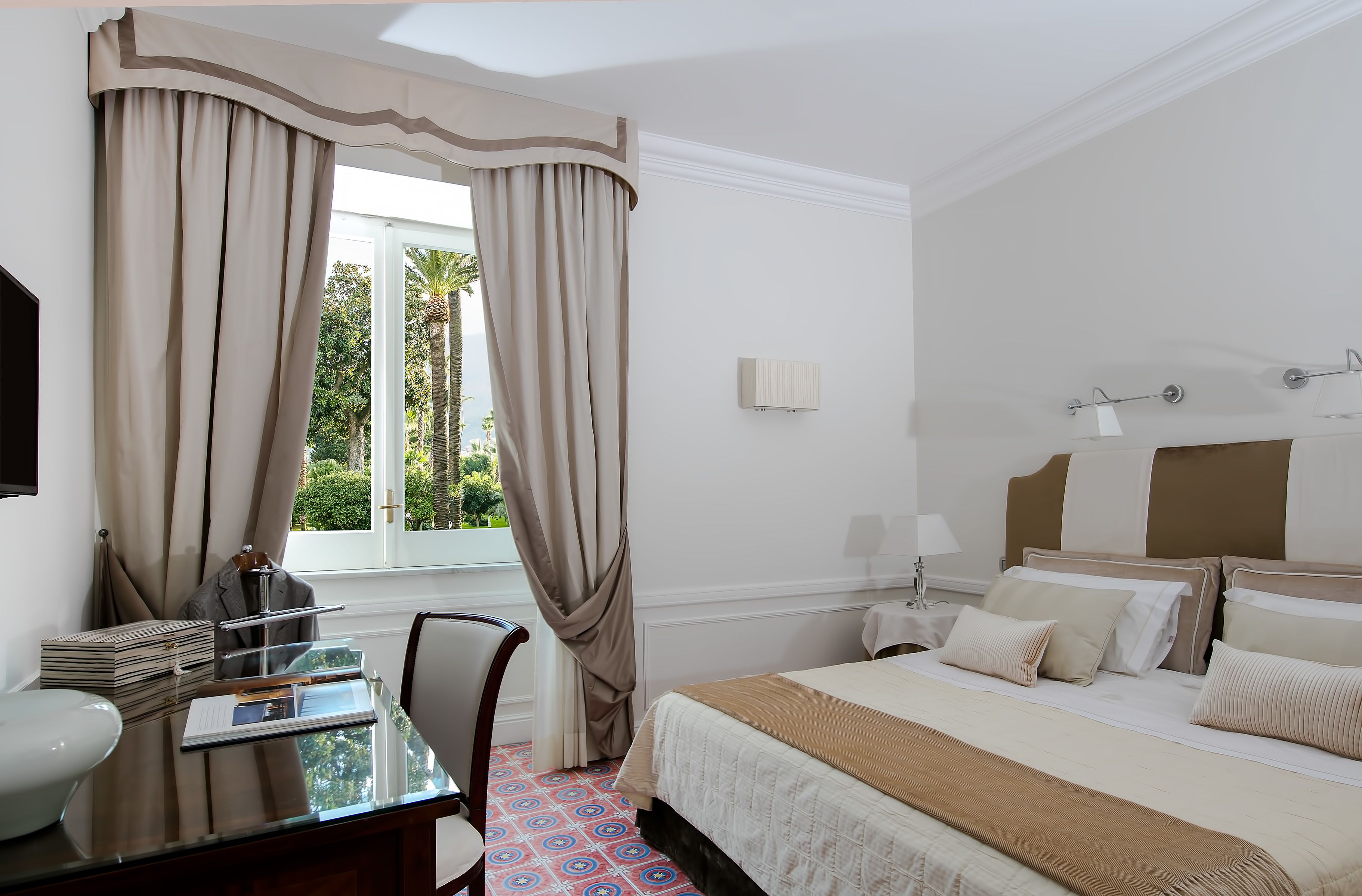 Una habitación de hotel con una cama, un escritorio y un ventanal con cortinas.