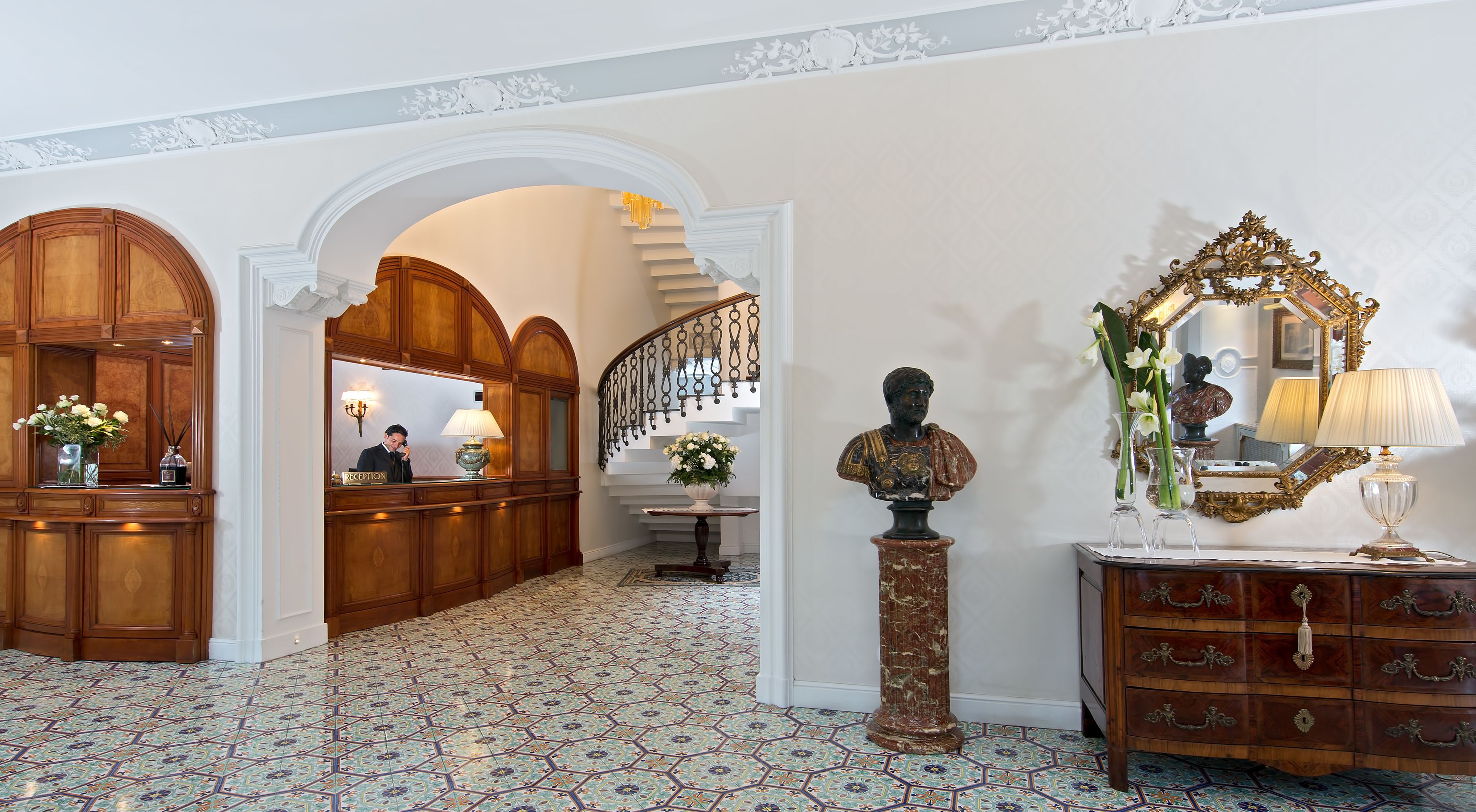 Ein Empfangsbereich mit einem Holztisch, einer Rezeptionistin und einer Treppe, die zu einer oberen Etage führt.