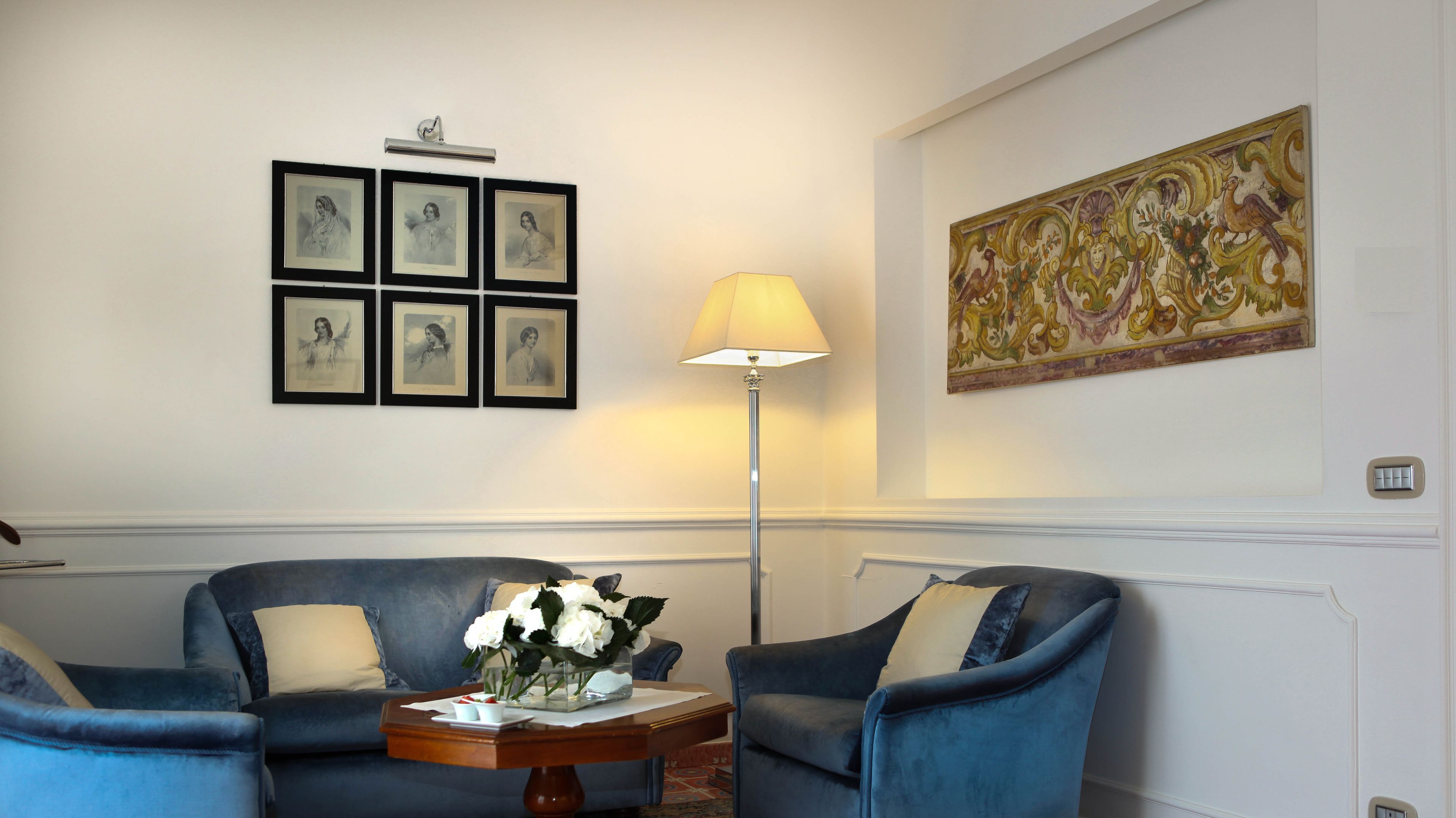 Una habitación con un sofá azul, una lámpara de pie y una obra de arte enmarcada en la pared.
