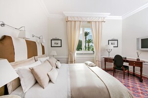 Habitación de hotel con una cama grande, un escritorio y una silla. Hay una ventana con cortinas, una lámpara y un marco de fotos en la pared.