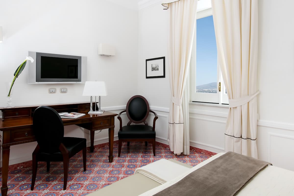 A hotel room with a bed, a desk with a chair, a television, and a window with curtains.