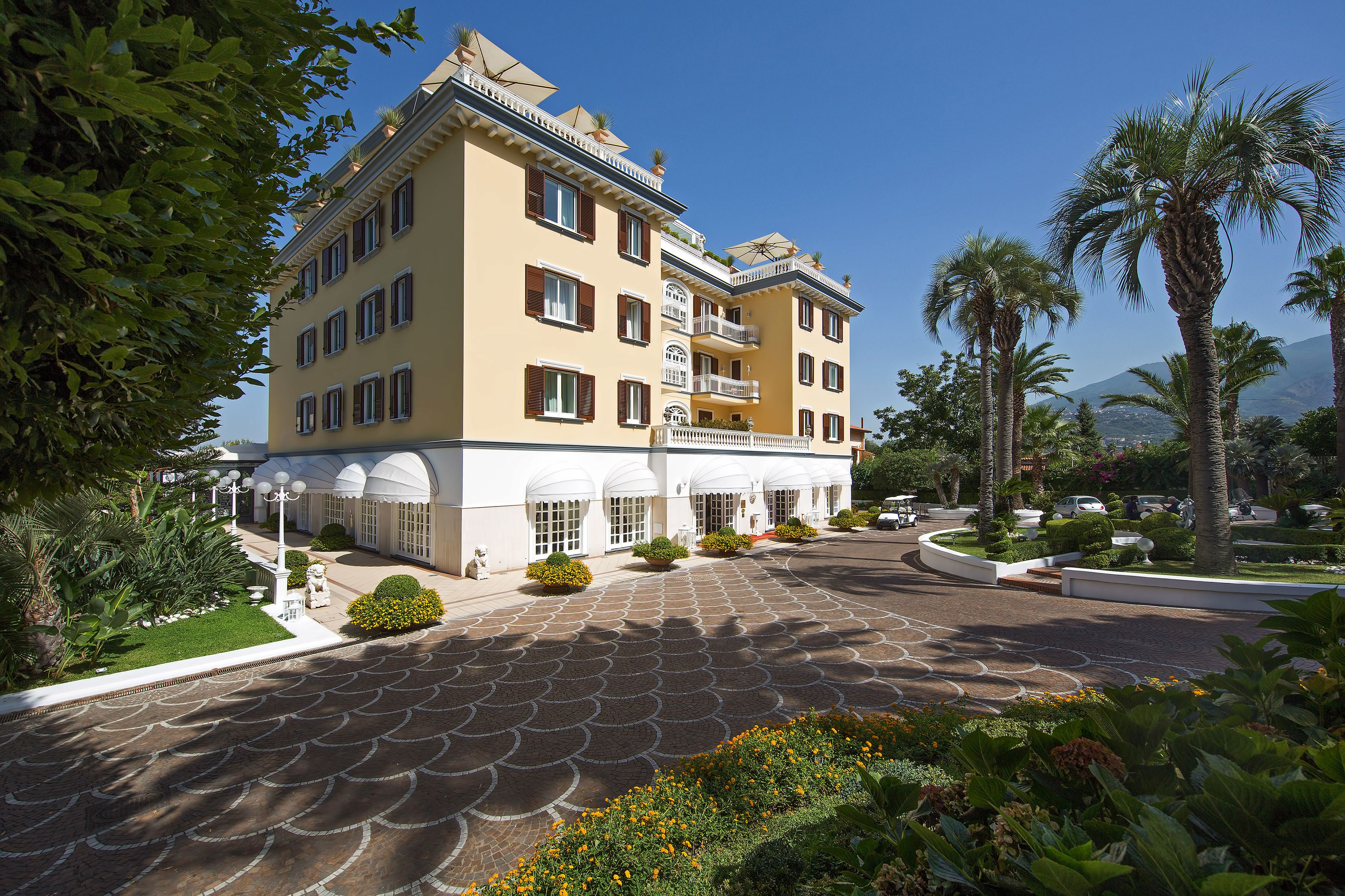 Ein mehrstöckiges Hotel mit Innenhof, Palmen und einem Berg im Hintergrund.