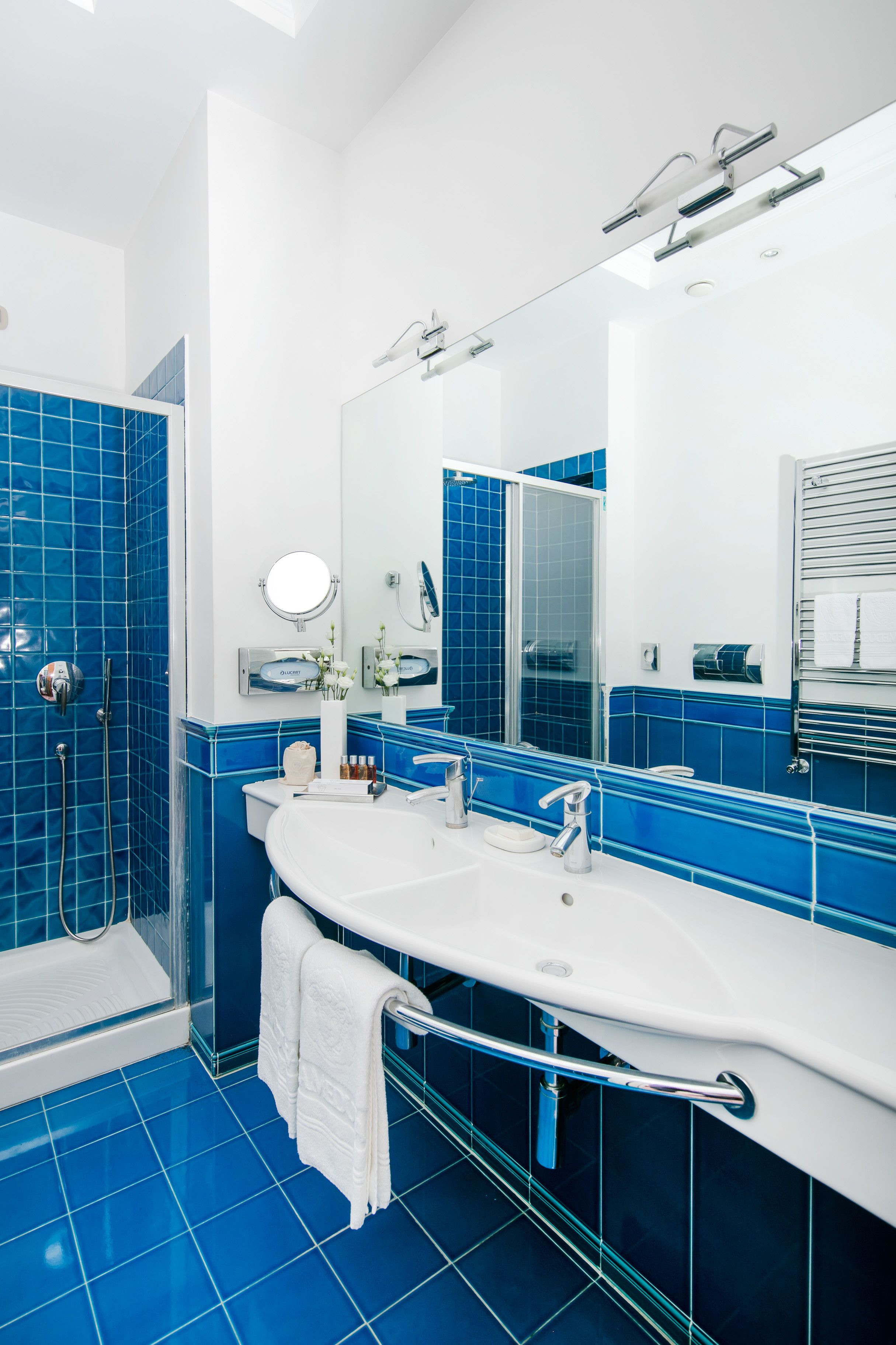 Une salle de bain moderne avec un grand lavabo, un miroir et une zone de douche carrelée de carreaux bleus.