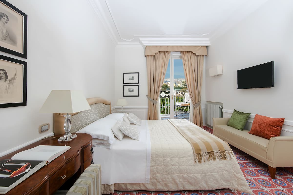 A hotel room with a bed, bedside table, lamp, and a sofa.