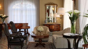 A room with a grand piano, a round wooden table, two armchairs, a sofa, and a large mirror.