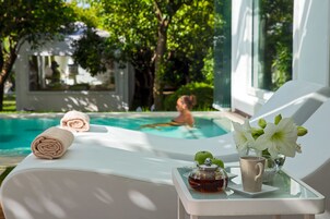 Un área de descanso junto a la piscina con vistas a ella, una mesa de vidrio con una tetera y una taza, y una silla con una toalla.