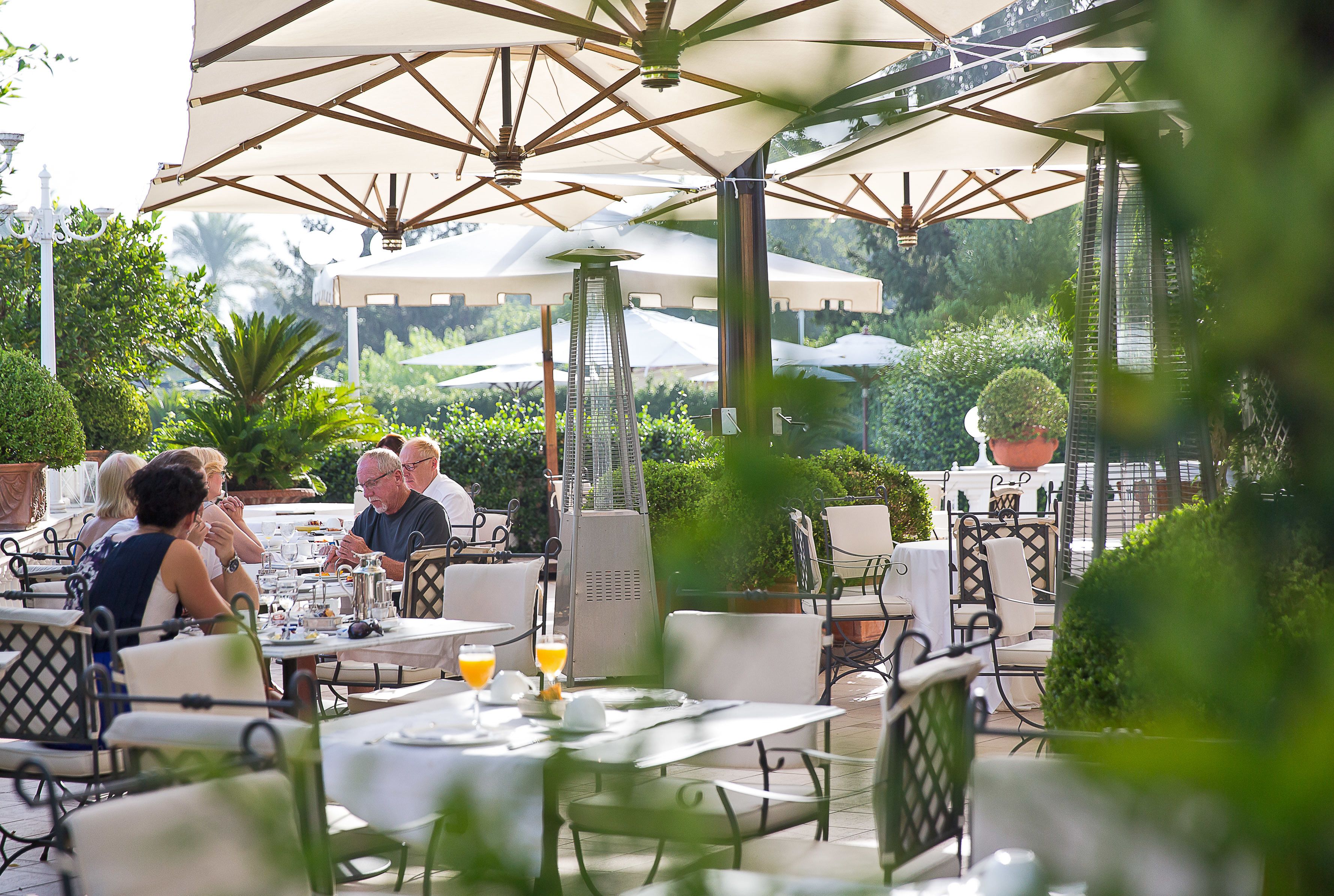 An outdoor dining area with tables and chairs, umbrellas, and potted plants.