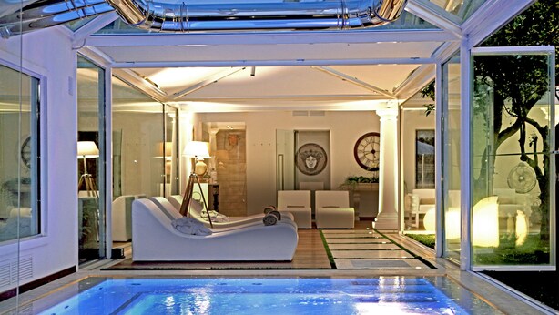 A modern indoor pool area with a lounge chair, a glass-enclosed room with a bed, and a view of the outdoors. - La Medusa Dimora di Charme (Castellammare di Stabia)
