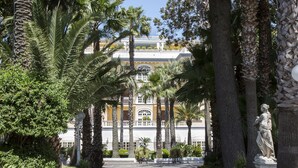A pathway lined with palm trees leading to a building with a white facade and a balcony. - La Medusa Dimora di Charme (Castellammare di Stabia)