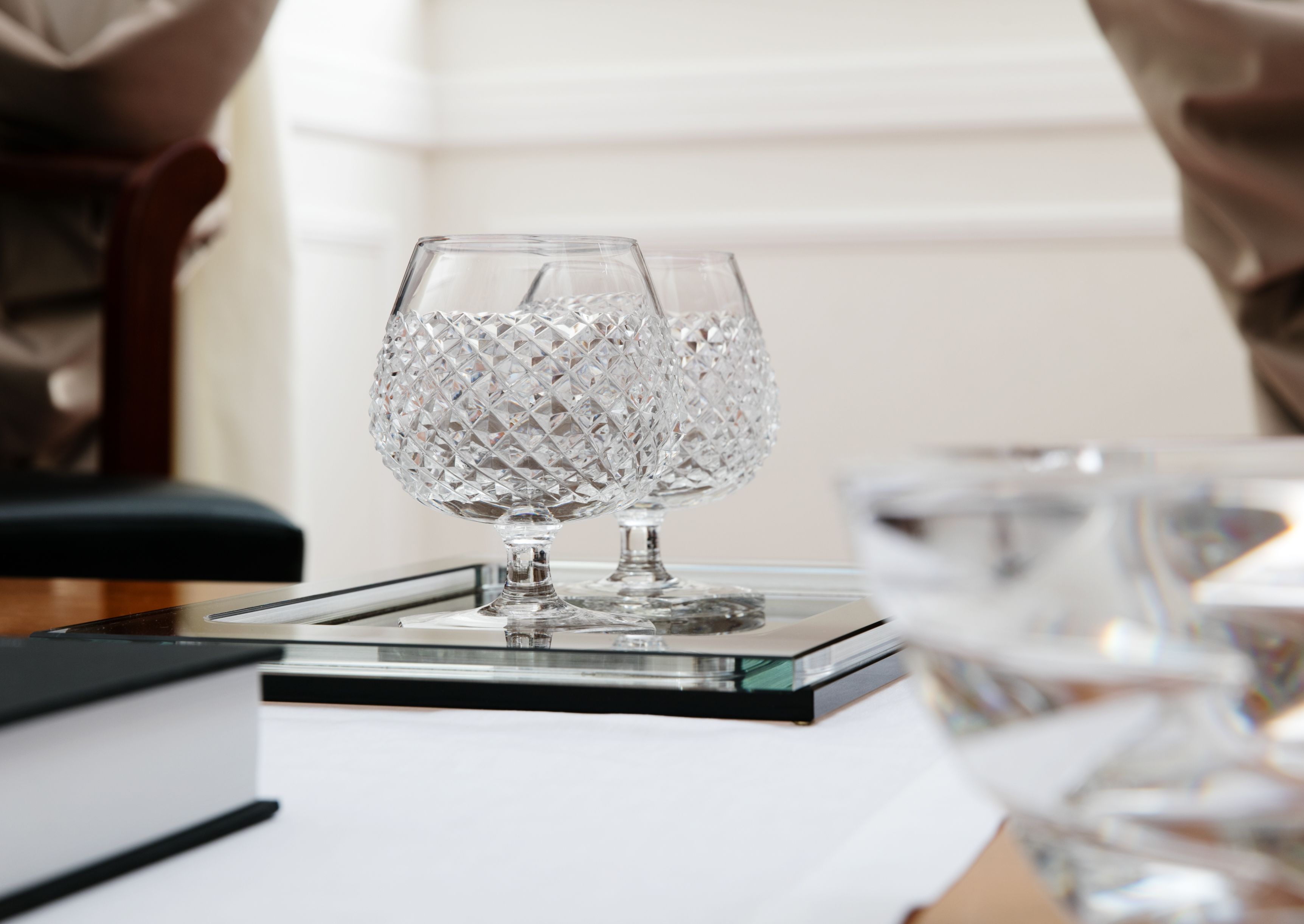 A clear glass goblet on a glass coaster, with a book and another glass nearby.