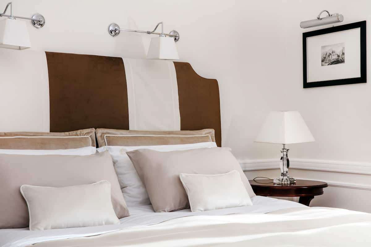 A neatly made bed with white linens and multiple pillows, a bedside table with a lamp, and a framed picture on the wall.