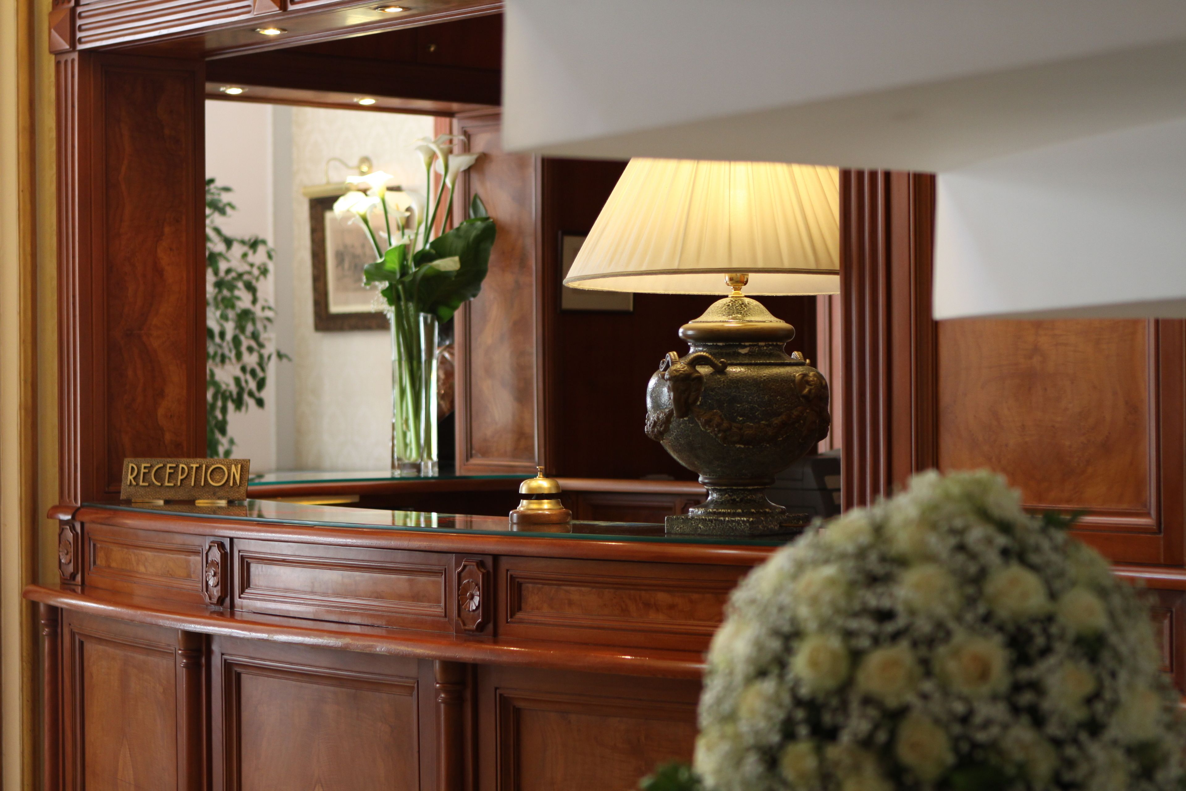 A reception desk with a lamp, a sign reading "RECEPTION", and a vase with flowers.