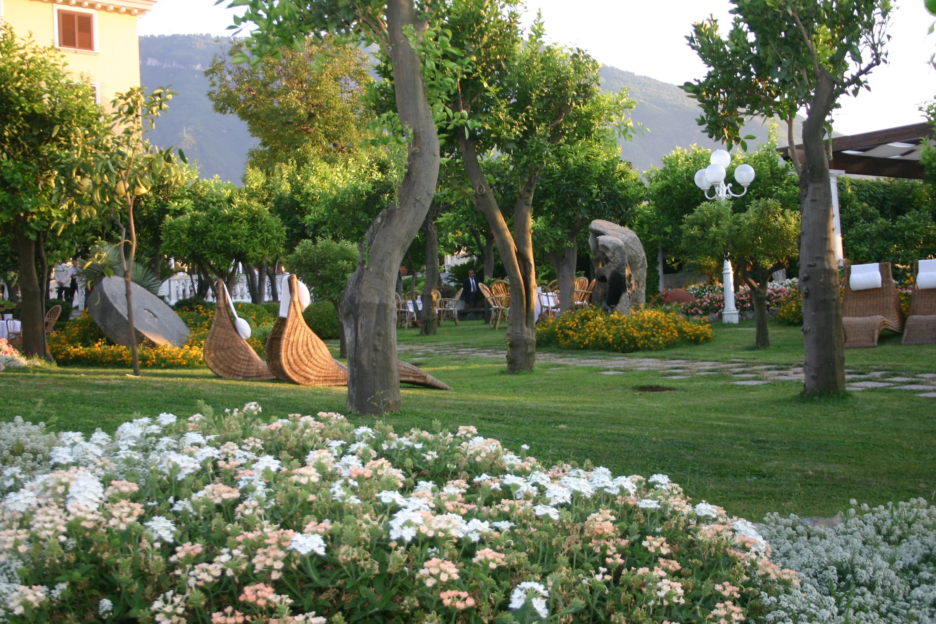 A garden with a variety of trees, a large rock sculpture, and a seating area with chairs.