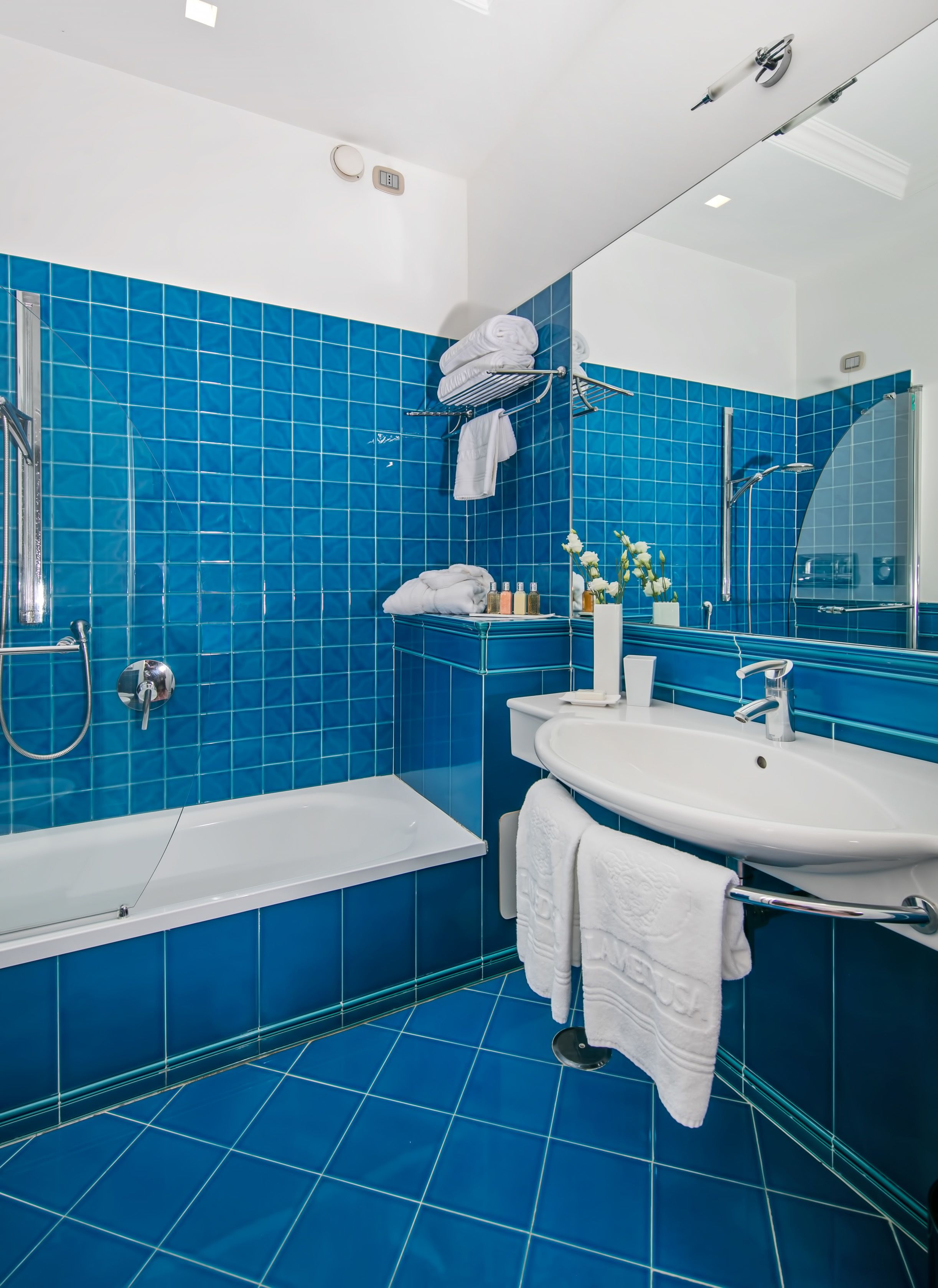A modern bathroom with blue tiles, a bathtub, a shower, and a sink with a mirror.