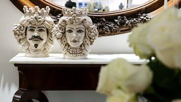Dos bustos de cerámica ornamentados sobre una mesa de mármol blanco, con un espejo que refleja una habitación.