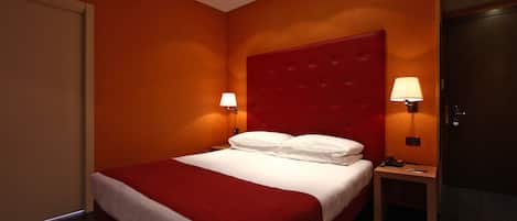 A hotel room with a red bedspread, a tufted headboard, two bedside lamps, and a wooden nightstand.
