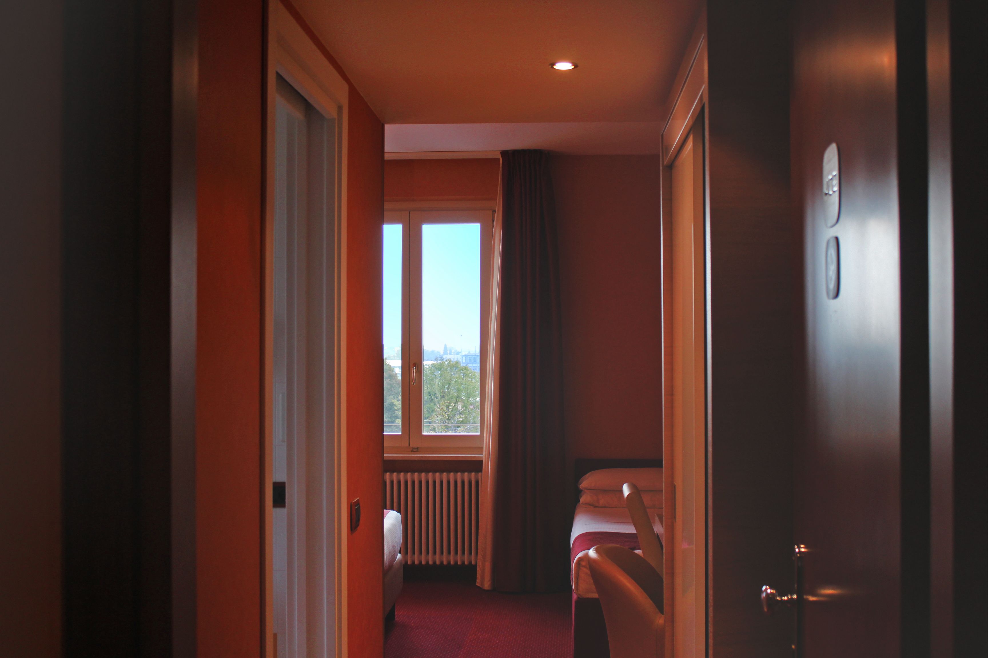 A hotel corridor with a bed, a radiator, and a window with curtains.