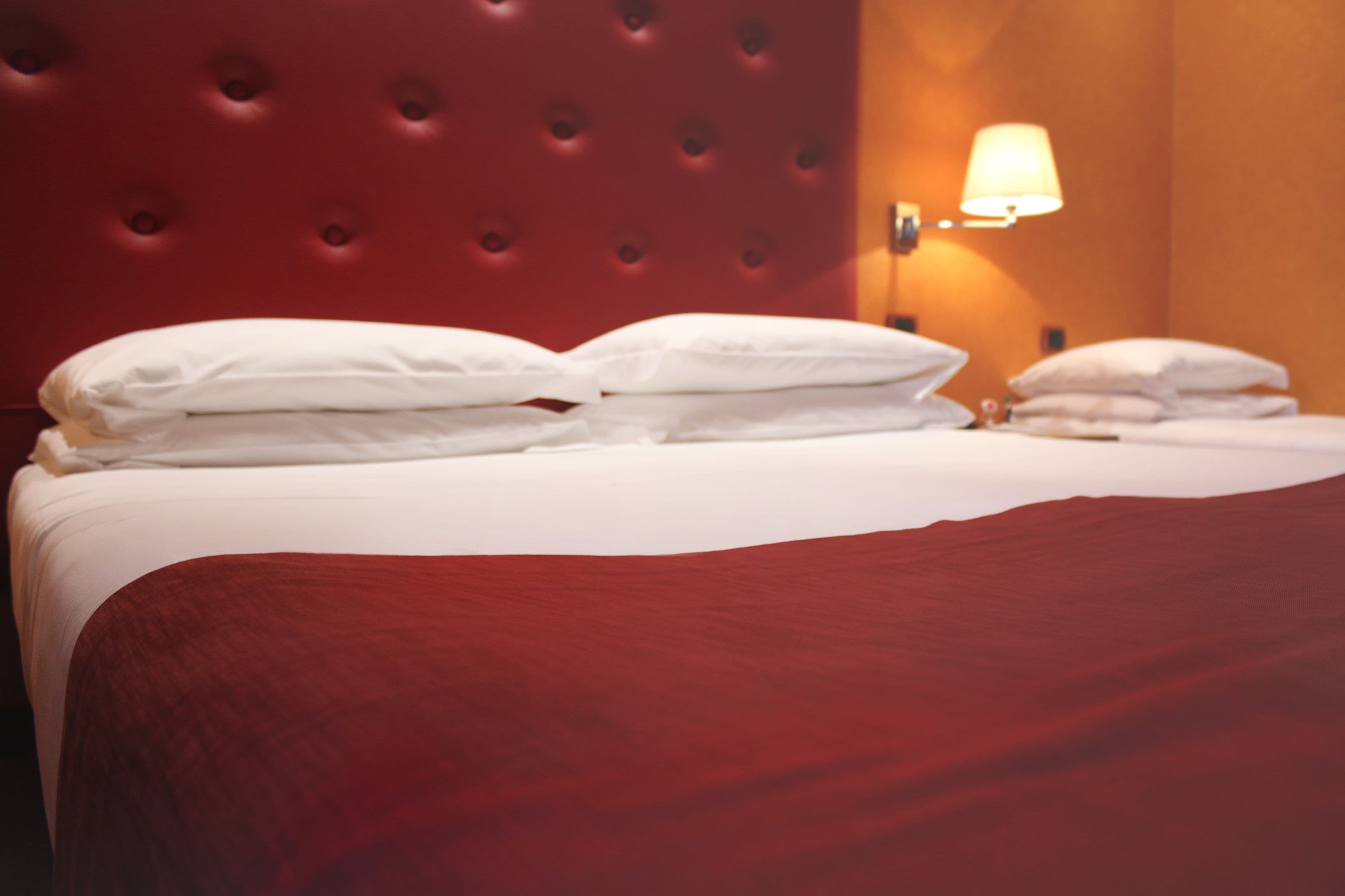 A neatly made bed with white linens and a red headboard.