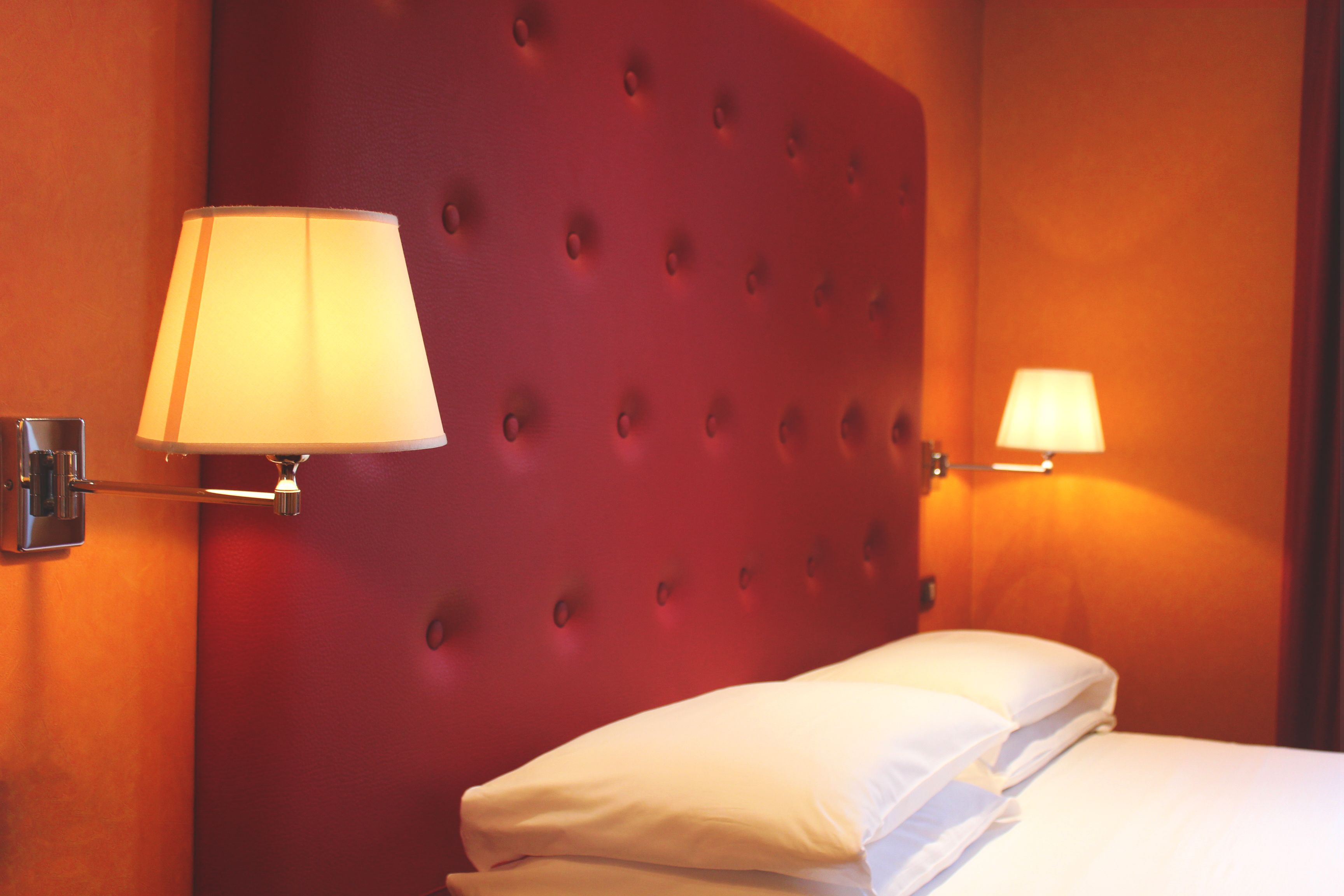 Una habitación de hotel con un cabecero capitonado, dos lámparas de noche y camas bien hechas.